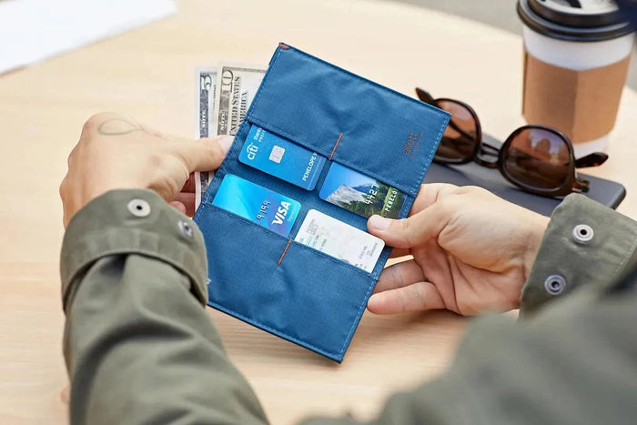 The ALLETT - THE ORIGINAL WALLET in RFID-blocking indigo blue nylon features four card slots, a cash pocket, and an orange no-slip card grip detail shown in a close-up inset. Text below reads "no-slip card grip.