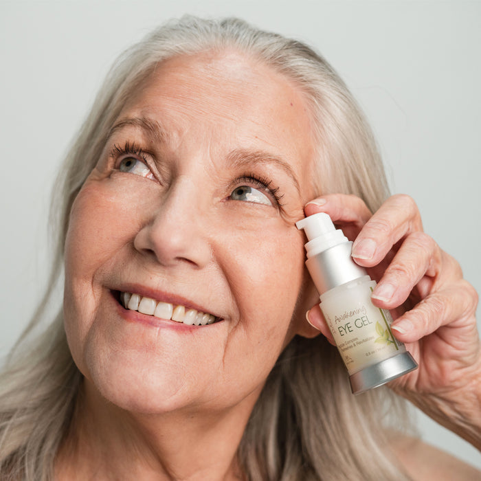 A woman holding the pump bottle Awakening Eye Gel near her eye