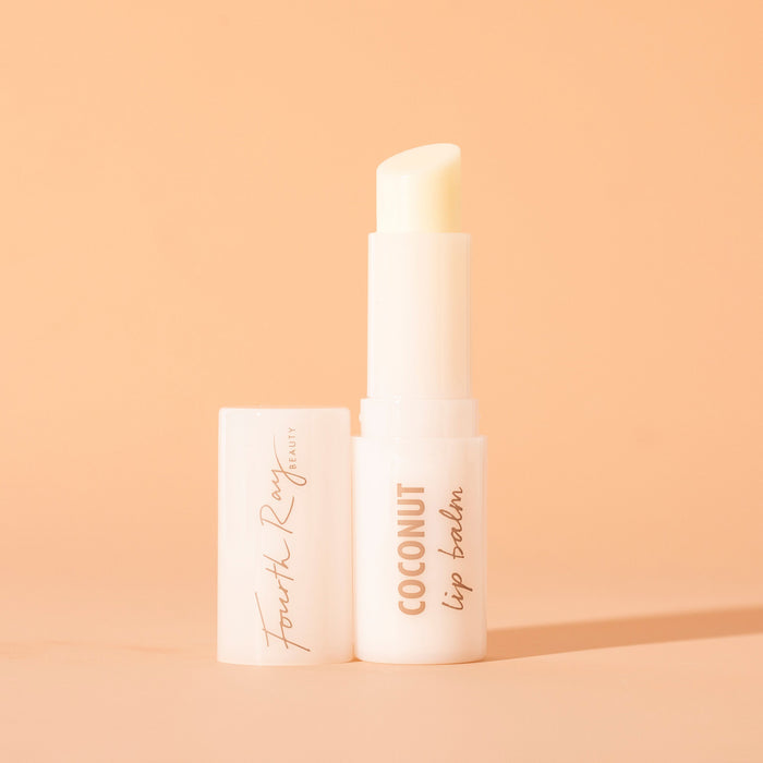 ColourPop Fourth Ray Beauty Coconut lip balm standing uncapped, creamy balm bullet exposed in a glossy white tube labeled COCONUT lip balm, cap beside it, on a warm peach background with soft shadow.