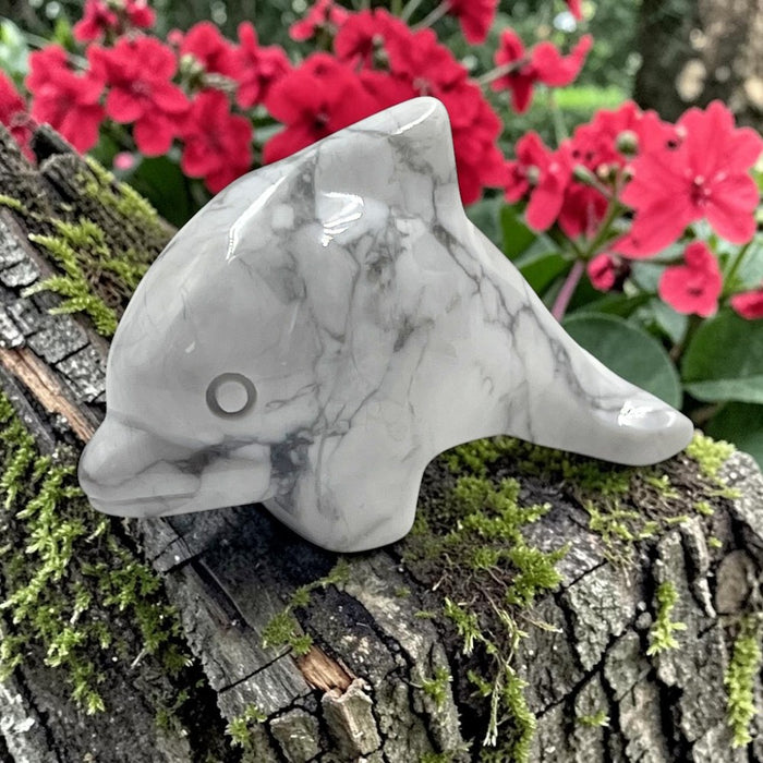 Howlite dolphin figurine on a tree branch with pink flowers in the background
