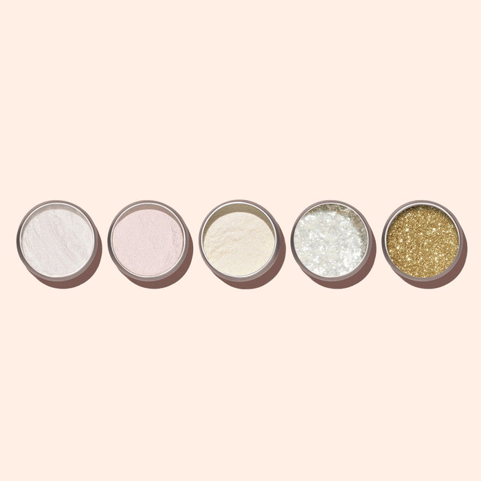 Five small round Manucurist Golden Glazed Effect Powder containers—white, light pink, beige, iridescent white, and pearly gold shimmer—are lined up horizontally on a pale beige background, perfect for achieving a stunning manicure look.