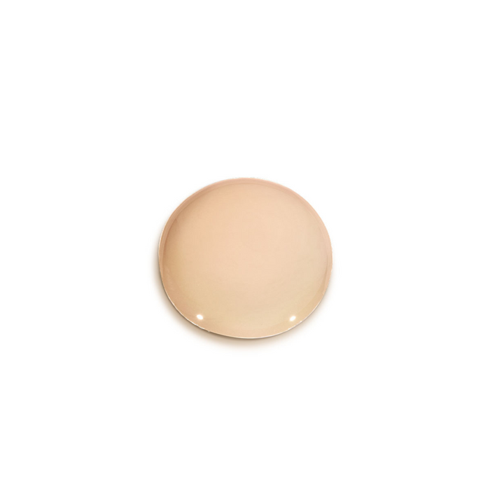 A smooth, circular cosmetic dollop swatch of Ayuna Velo skincare, showcasing its creamy, light peach-toned tint.