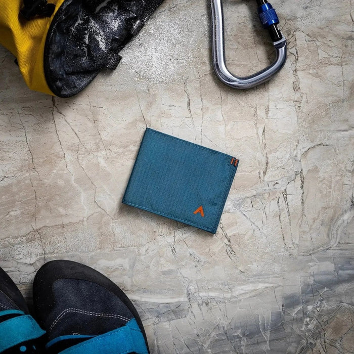 The ALLETT Sport Wallet in RFID-blocking indigo blue nylon features a minimalist design with an orange triangular logo on the corner, shown against a white background.