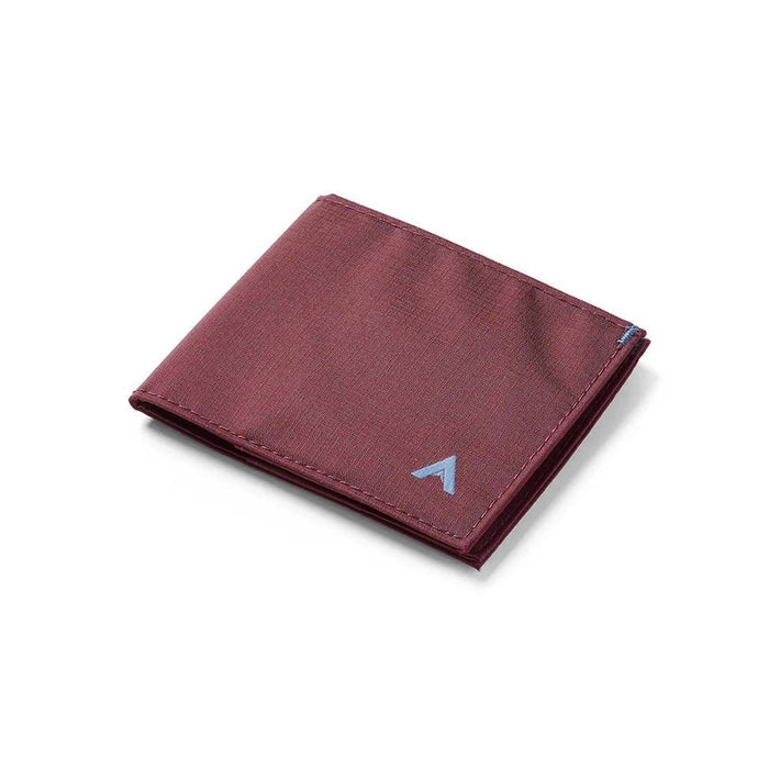 An ALLETT Sport Wallet in RFID-blocking mulberry nylon, along with a pen, sunglasses, candle, seashell, iPhone, and AirPods are neatly displayed on a marble surface.