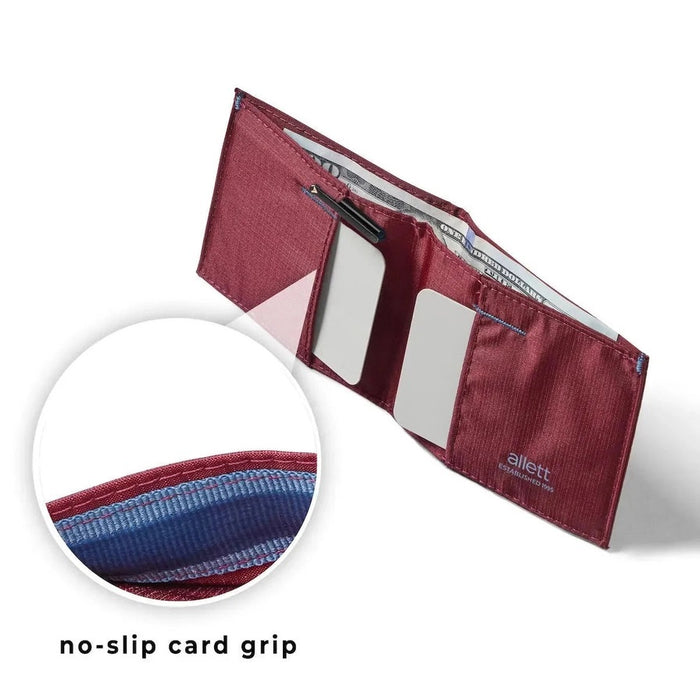 An ALLETT Sport Wallet in RFID-blocking mulberry nylon, along with a pen, sunglasses, candle, seashell, iPhone, and AirPods are neatly displayed on a marble surface.