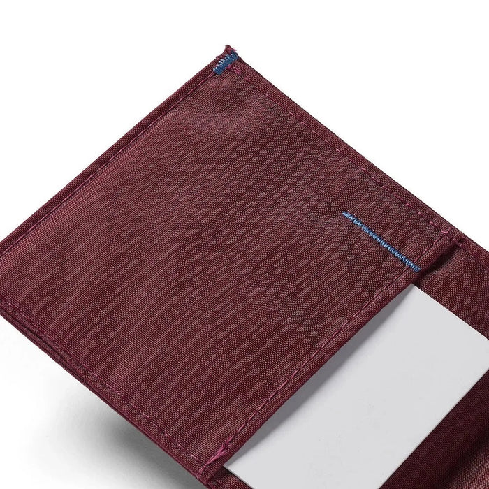 An ALLETT Sport Wallet in RFID-blocking mulberry nylon, along with a pen, sunglasses, candle, seashell, iPhone, and AirPods are neatly displayed on a marble surface.