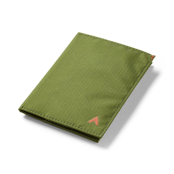 A Cala Green ALLETT RFID-blocking nylon wallet rests on a wooden surface beside a green notebook, portable stove, headlamp, black bag, pocket knife, camping gear, and round dark objects.