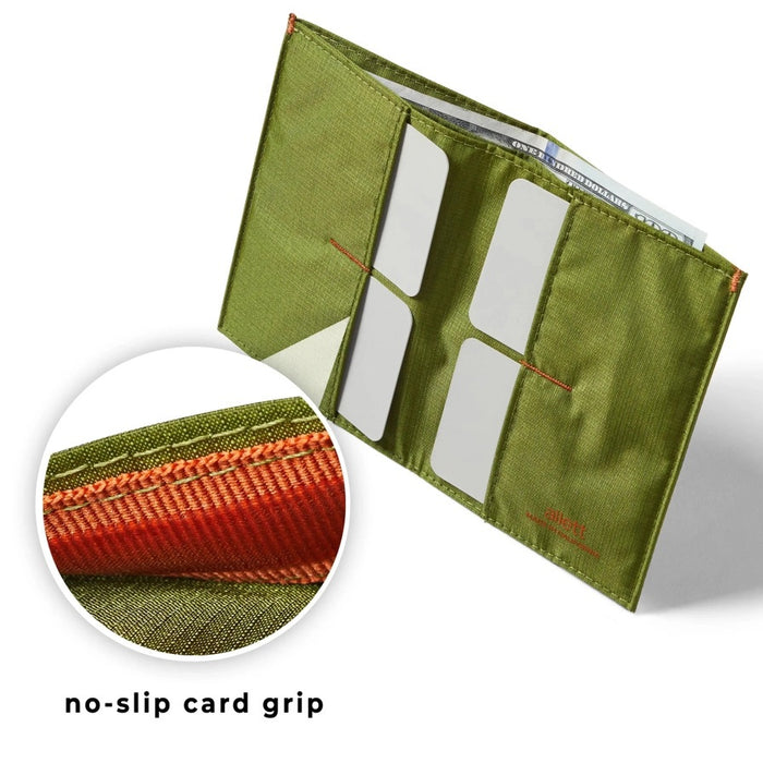 A Cala Green ALLETT RFID-blocking nylon wallet rests on a wooden surface beside a green notebook, portable stove, headlamp, black bag, pocket knife, camping gear, and round dark objects.