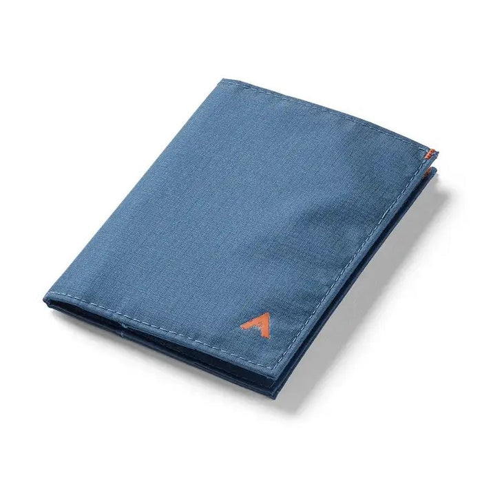 The ALLETT - THE ORIGINAL WALLET in RFID-blocking indigo blue nylon features four card slots, a cash pocket, and an orange no-slip card grip detail shown in a close-up inset. Text below reads "no-slip card grip.