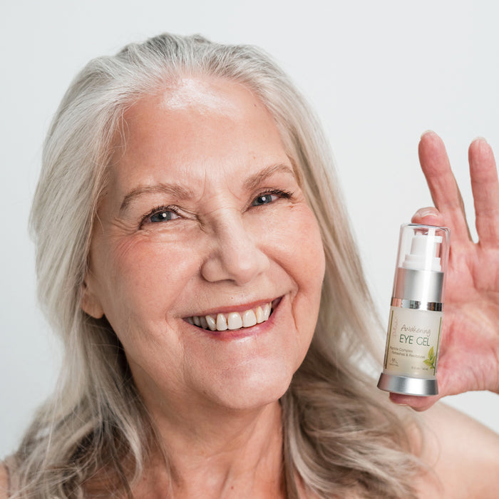 A closeup of a woman's face holding a pump bottle of Awakening Eye Gel