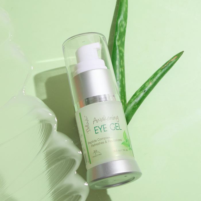 A pump bottle of Awakening Eye Gel  with a swatch of gel and two aloe plant leaves from a bird's eye view