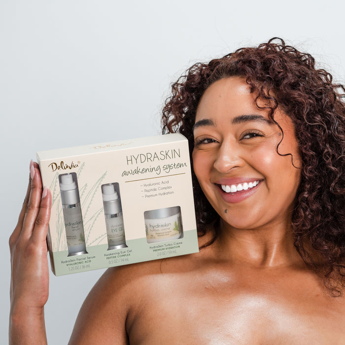 Smiling woman holding Deluvia HydraSkin Awakening Anti-Aging System on her shoulder