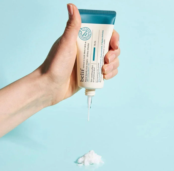 Hand squeezing belif Aqua Bomb Cica Cream moisturizer from tube onto blue surface