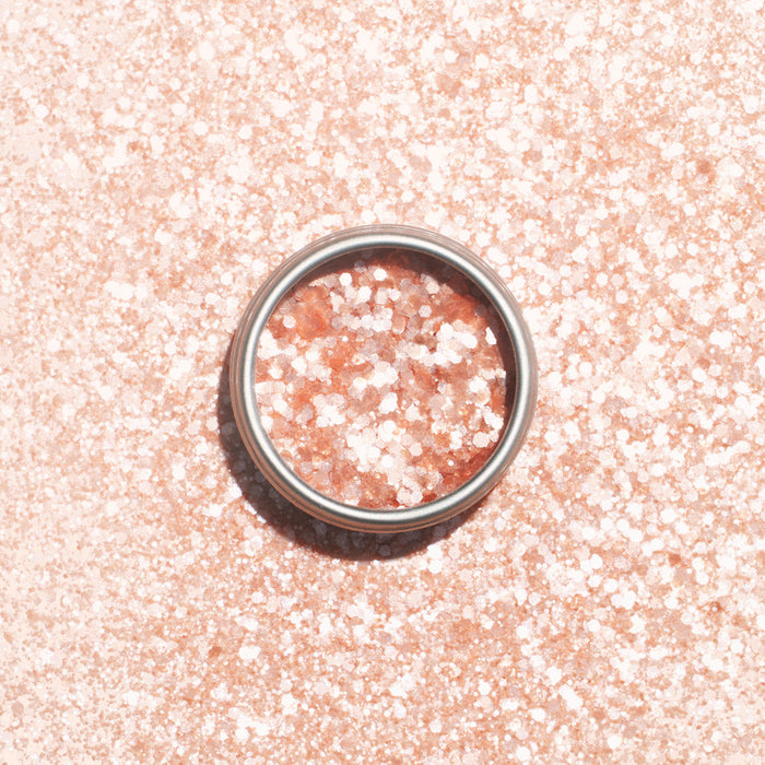 A silver ring rests on a pale pink surface dusted with Manucurist’s Blush Biodegradable Glitter, shimmering through the ring and all around it.