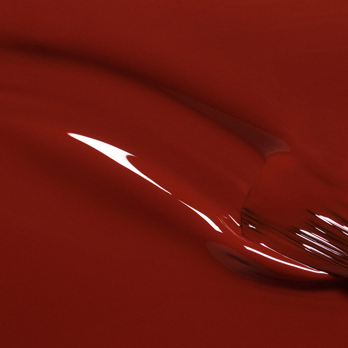 Close-up of Bohème by Manucurist—a glossy, smooth red surface with brown undertones and curved reflections, reminiscent of red polish for an abstract, fluid look.
