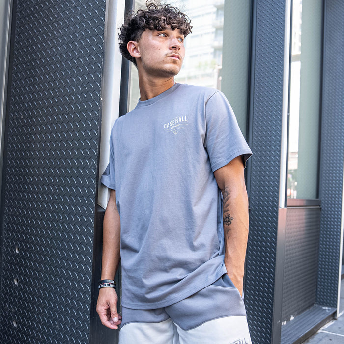 Man wearing a light gray t-shirt with text, standing against a textured wall.