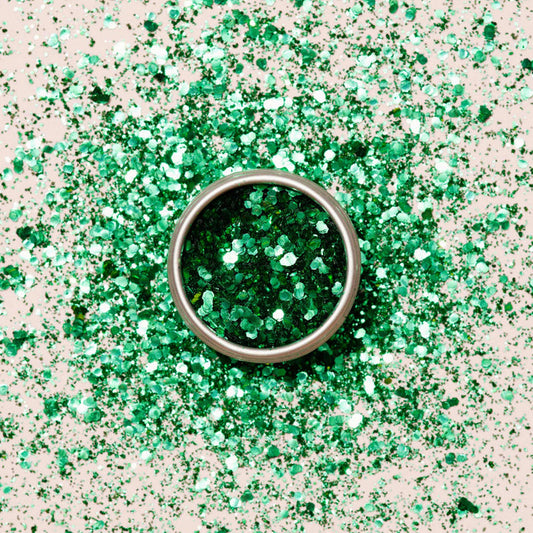 A round metal container of Manucurist Cactus Biodegradable Glitter sits on a surface, surrounded by scattered green glitter—perfect for creative nail art designs.