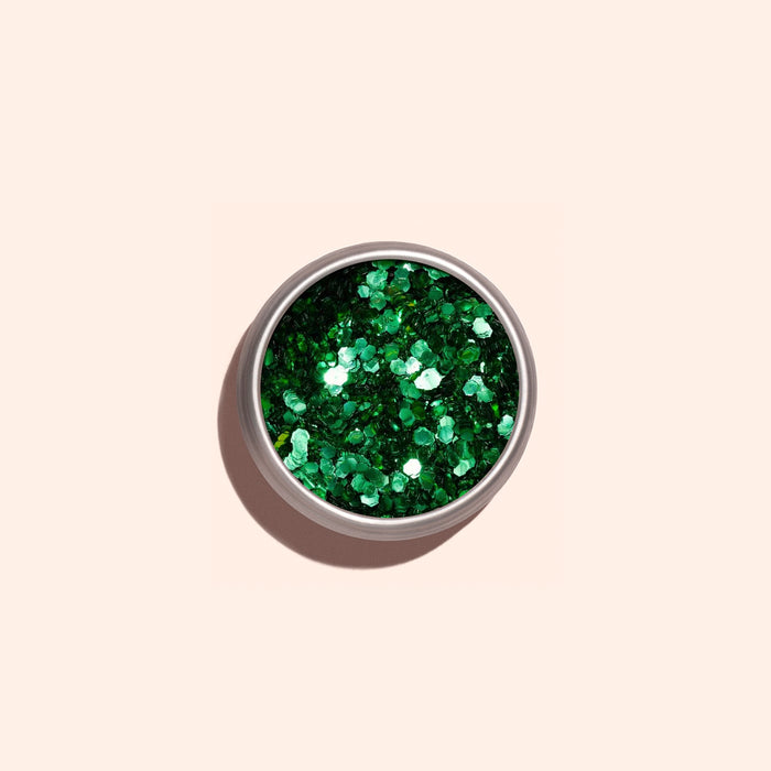 A small round container of Manucurist’s Cactus Biodegradable Glitter sits on a light beige background, its shiny green eco-friendly sparkles casting a soft shadow—ideal for sustainable nail art.