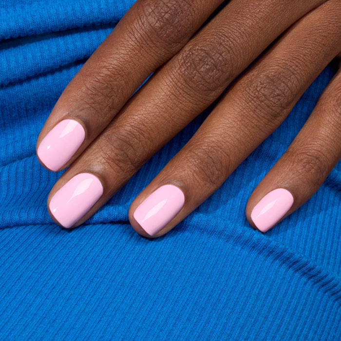 A close-up of a hand with neatly manicured nails painted in Manucurist’s Candy, a cool-toned LED light pink polish, resting on bright blue ribbed fabric.