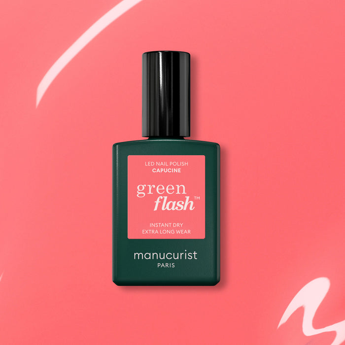 A dark green bottle of Manucurist Capucine Green Flash gel polish is displayed against a coral pink background with white curved accents.