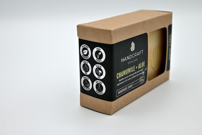 packaged white and yellow swirled chamomile and aloe soap in a Kraft box with a black label and white logos stating all natural ingredients, vegan friendly, cruelty free, palm oil free, sensitive skin friendly and non toxic ingredients