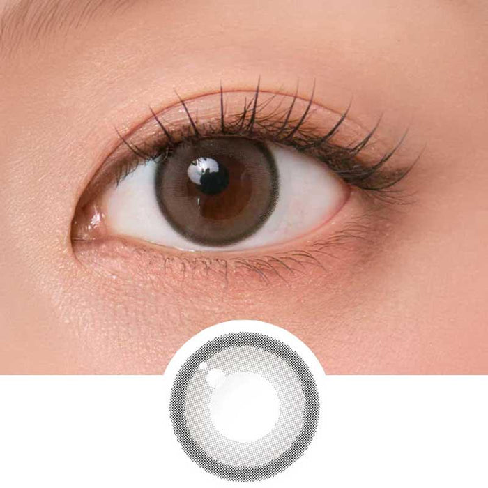 Close-up shot of model's eye adorned with Chuu Aery Rose Lucid Grey (10pk) daily color contact lenses with prescription, complemented by glittery eye makeup, showing the brightening and enlarging effect of the circle contact lens on dark brown eyes, above a cutout of the contact lens pattern with limbal ring on a white background.