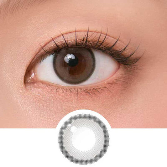 Close-up shot of model's eye adorned with Chuu Aery Rose Lucid Grey (10pk) daily color contact lenses with prescription, complemented by glittery eye makeup, showing the brightening and enlarging effect of the circle contact lens on dark brown eyes, above a cutout of the contact lens pattern with limbal ring on a white background.