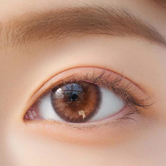 Close-up shot of model's eye adorned with Chuu Cloud Pudding Pink Brown (10pk) color contact lenses with prescription, complemented by minimalist eye makeup, showing the brightening and enlarging effect of the circle contact lens on dark brown eyes.