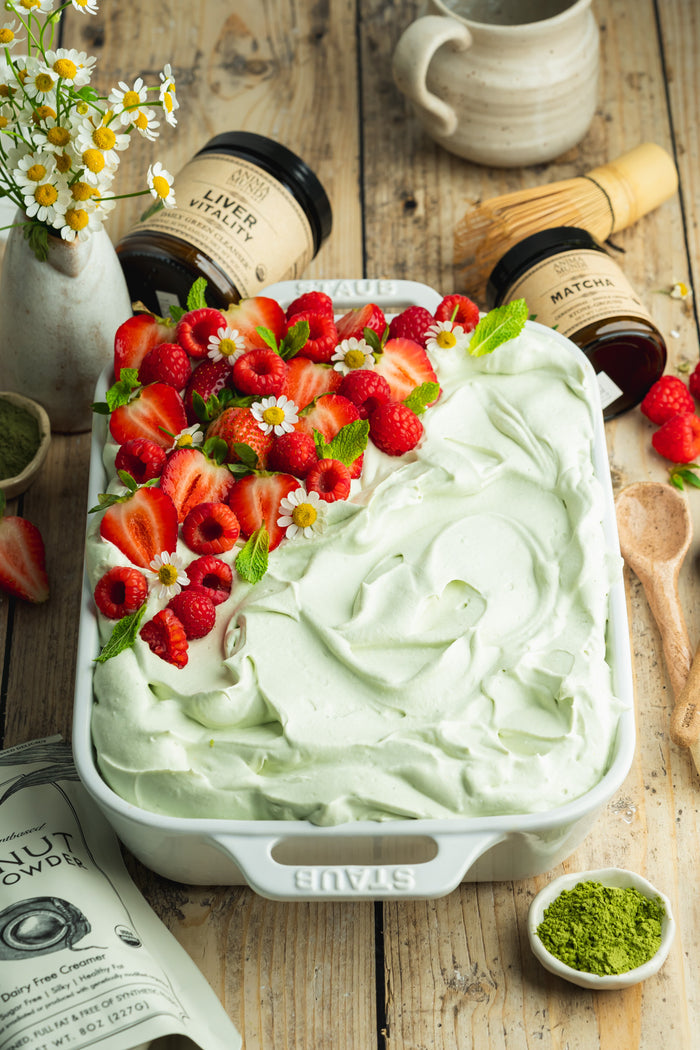 Green dessert with strawberries on a wooden table with matcha ingredients.