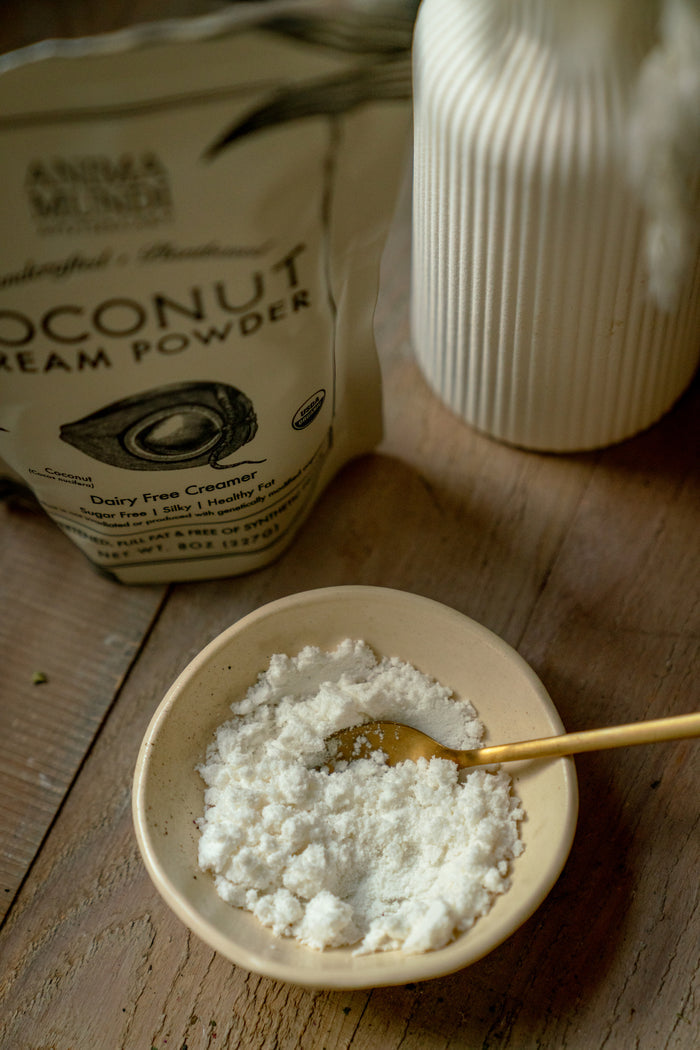 Coconut cream powder in a bowl with a spoon, next to a container of the product on a wooden surface.