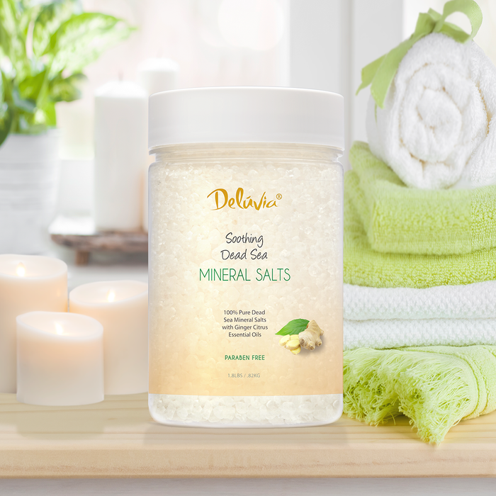 Jar of Deluvia Dead Sea Mineral Salts Unscented on a bathroom counter with towels and candles.