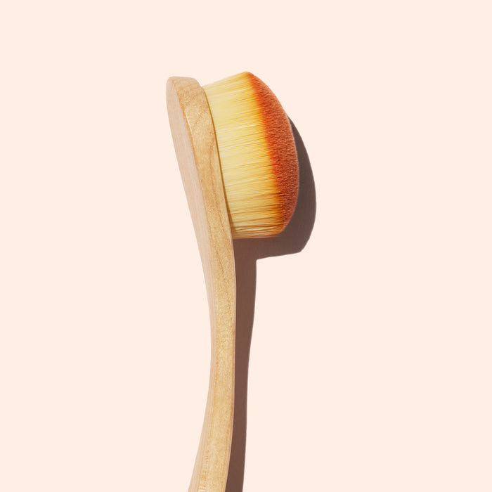 The Manucurist Dust Brush features a wooden handle, dense light vegan bristles, and a slightly rounded head, perfect for manicure care, shown against a pale beige background.