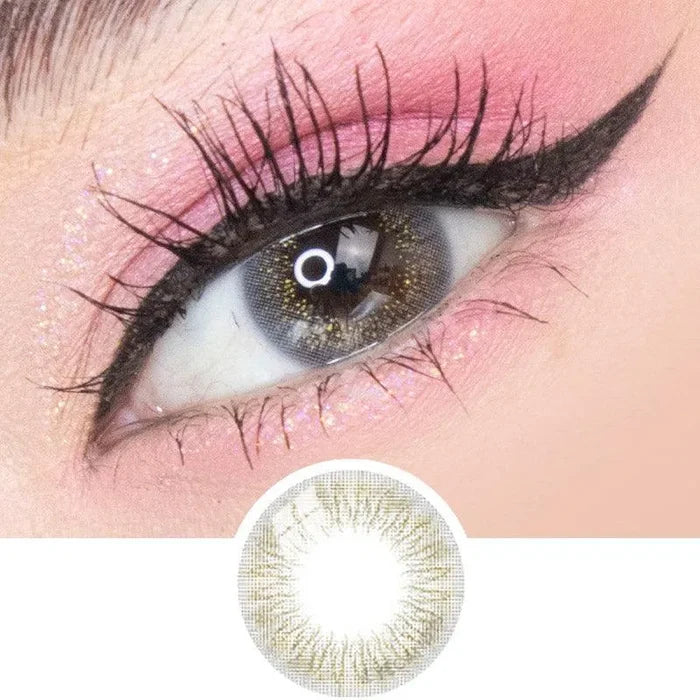 A close-up of an eye with dramatic black eyeliner, long lashes, pink eyeshadow, and glitter, wearing EyeCandys Attitude Glitter Grey colored contacts by EyeCandys with a subtle gold and brown pattern shown in detail below.