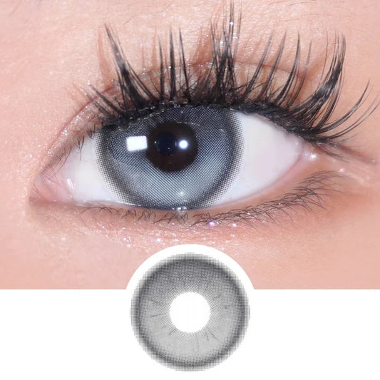 A close-up of an eye wearing EyeCandys Bunnie Milky Ash Grey lenses shows long lashes. Below, an enlarged image highlights the EyeCandys lens' glowy ash grey pattern and detailed design.