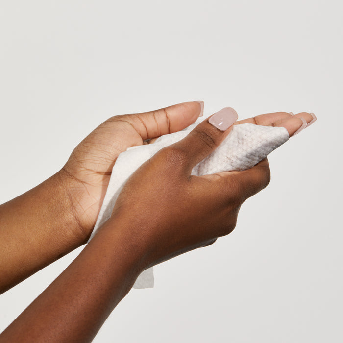 Up close shot of 2 hands using Beekman 1802's Glacial Mint & Eucalyptus Face Wipes to clean themselves, on a white background.