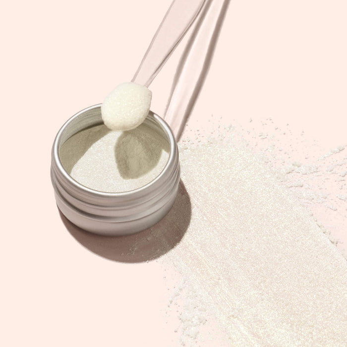 An open container of Manucurist Golden Glazed Effect Powder sits on a light pink surface, its pearly gold shimmer catching the light. A small applicator and a touch of spilled powder make it perfect for adding brilliance to any manicure.