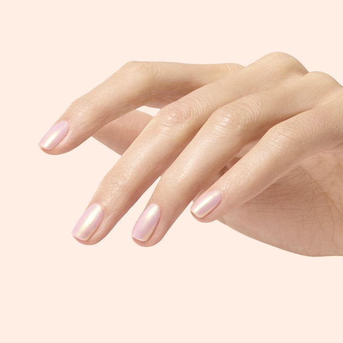 A close-up of a flawless manicure showcases nails coated in Manucurist Golden Glazed Effect Powder, a light pearly pink with golden shimmer, set against a soft beige background.