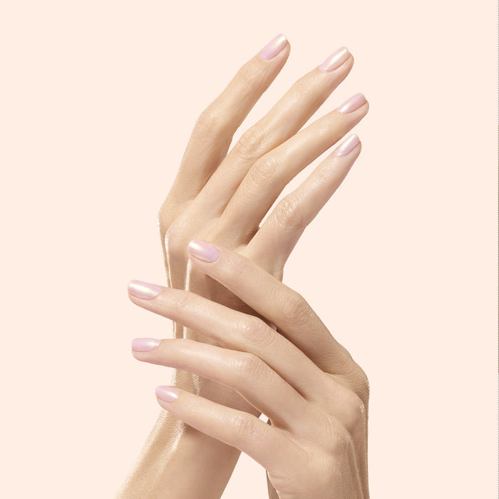 Two hands with perfectly manicured, neatly shaped nails coated in Manucurist’s Golden Glazed Effect Powder gently touch each other, showcasing a light pink hue with pearly gold shimmer against a soft beige background.