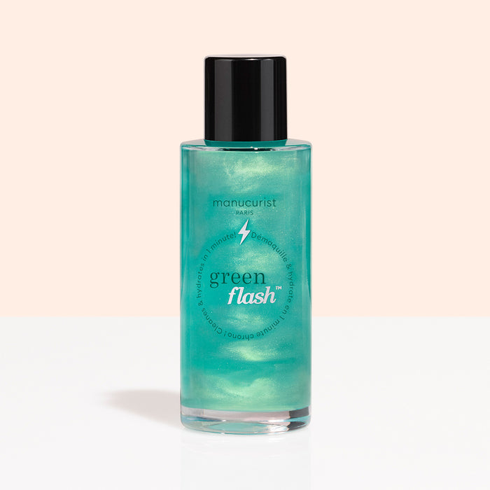 A clear bottle with a black cap, labeled “Manucurist Green Flash™ Gentle Glitter Remover,” holds shimmery teal, acetone-free liquid and is displayed against a light peach and white background.