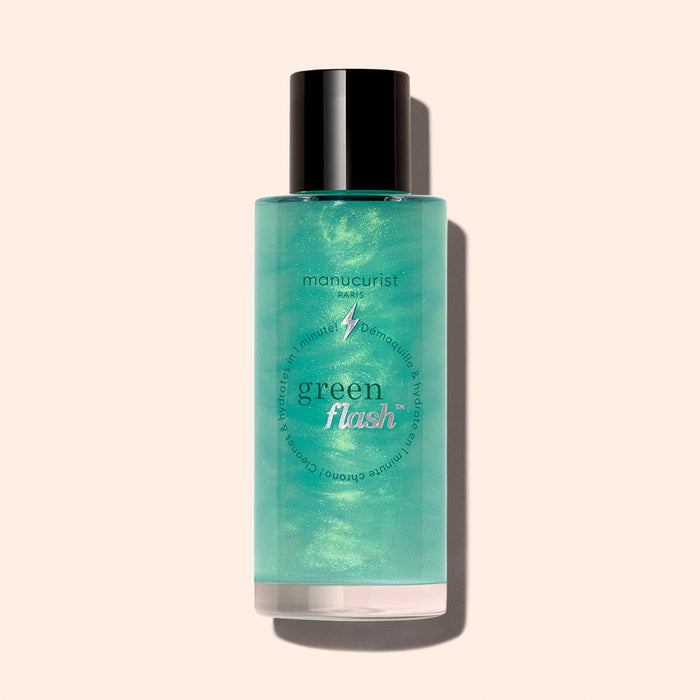 A bottle of Manucurist Green Flash™ Gentle Glitter Remover with a black cap, containing light green liquid, enriched with castor oil, is shown against a light beige background.