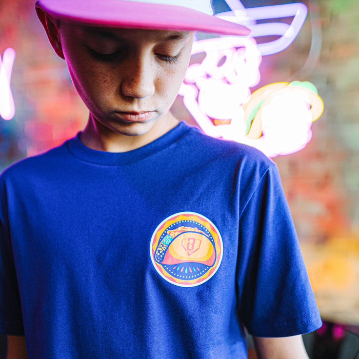 Person wearing a purple t-shirt with a colorful taco logo, standing against a neon-lit background.