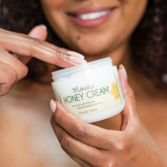 A woman dipping two fingers into an open jar of Manuka Honey Cream
