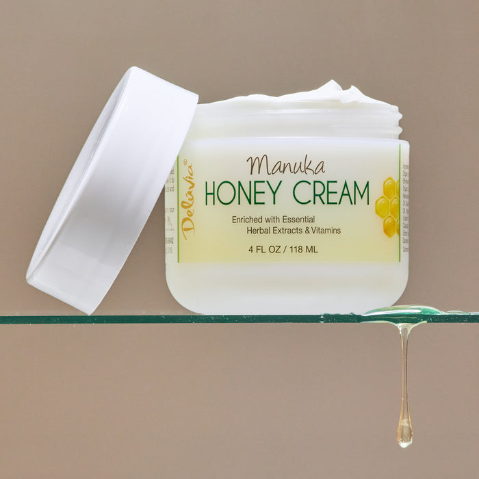 An open jar of Manuka Honey Cream on a glass shelf, with honey dripping off the shelf.