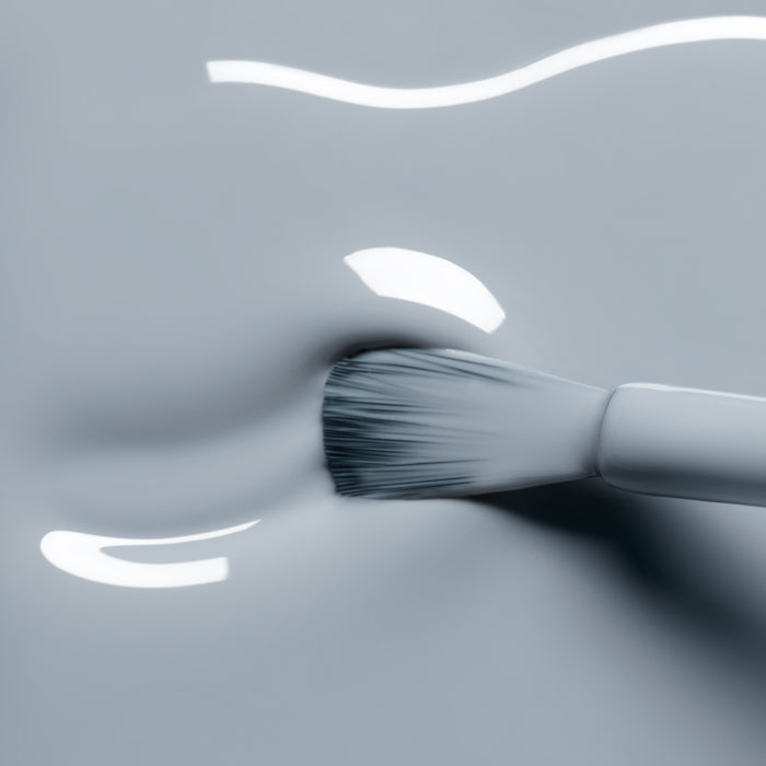 A close-up of a brush spreading Manucurist Mist Grey gel polish—its glossy, light gray shade shines with smooth, reflective texture.