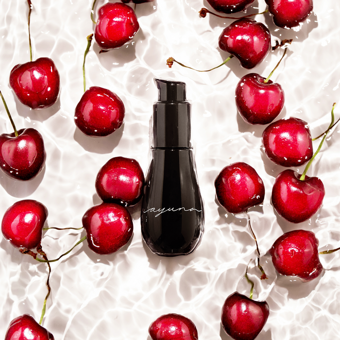 Black serum bottle surrounded by red cherries on a textured white background