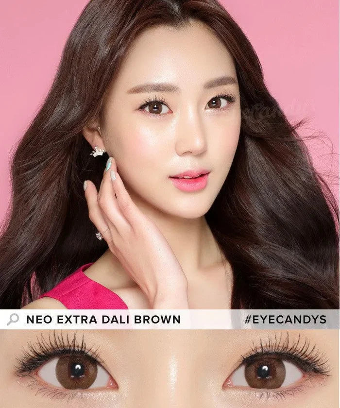 A woman with long, wavy dark hair poses against a pink background, wearing natural makeup and pink lipstick. A close-up highlights her brown eyes enhanced by NEO Vision Extra Dali Brown lenses. #EYECANDYS is displayed on the image.