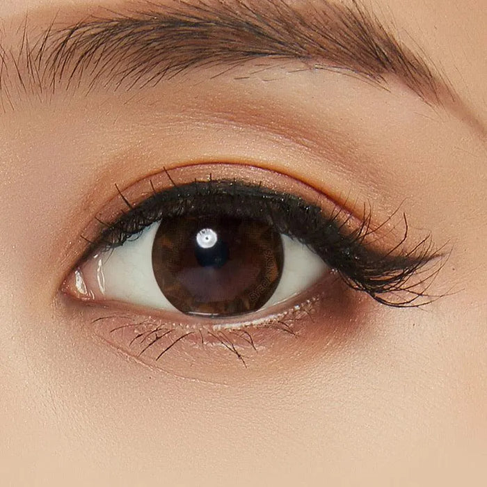 A close-up of a brown eye with long lashes, natural makeup, groomed brows, smooth light-toned skin, and NEO Vision Ruby Queen Brown (Custom Toric for Astigmatism) prescription colored contacts for a seamless look.