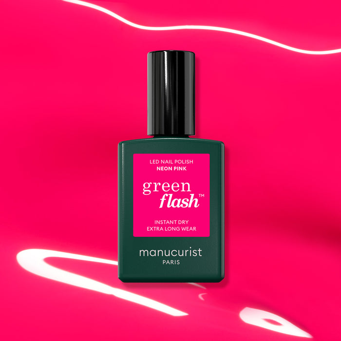 A bottle of Manucurist Neon Pink gel polish is displayed on a vibrant pink background with white light reflections, showcasing its ultra-shiny finish.