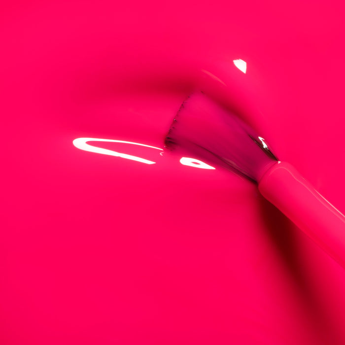 A close-up of a makeup brush resting on Manucurist's Neon Pink surface, showcasing its ultra-shiny, glossy finish as light reflects off the vibrant background.