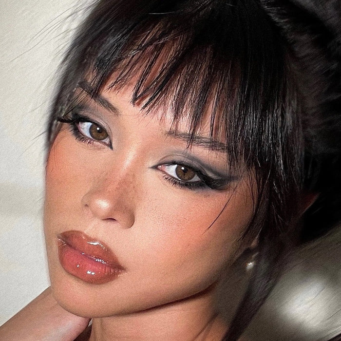 Smoky gray eyeshadow defines brown eyes, showcasing cool-toned quartz hues from the ColourPop Of Quartz shadow palette, paired with winged liner and glossy nude lips, in a tight beauty close-up with soft, warm lighting.